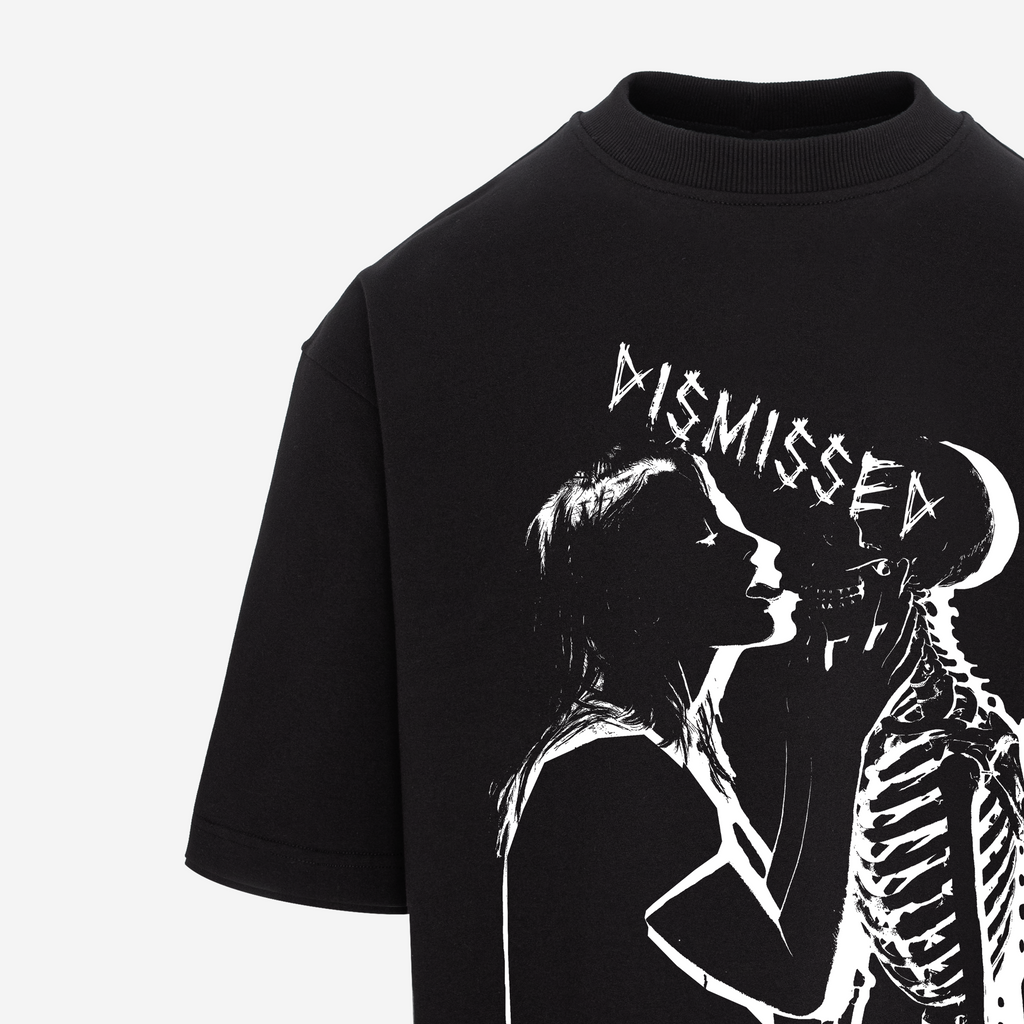 A close-up of a black short-sleeve t-shirt featuring a white graphic print of a woman kissing a skeleton, with the word 'DISMISSED' written above in a distressed font.